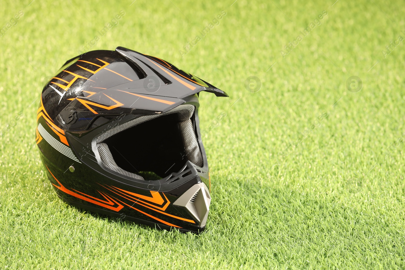 Photo of Modern motorcycle helmet with visor on green grass, space for text