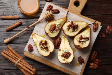 Photo of Tasty baked pears with nuts, blue cheese, thyme, honey and cinnamon sticks on wooden table, flat lay