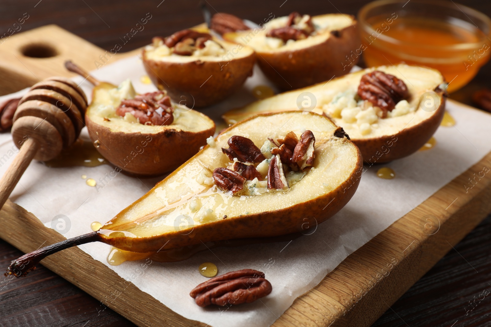 Photo of Tasty baked pears with nuts, blue cheese, thyme and honey on wooden table, closeup