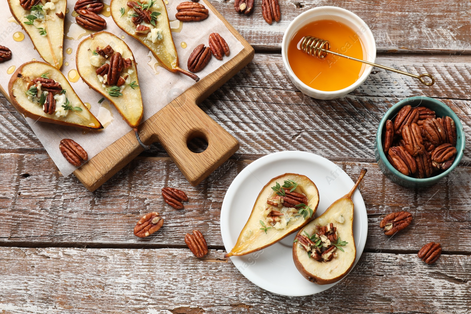 Photo of Tasty baked pears with nuts, blue cheese, thyme and honey on wooden table, flat lay