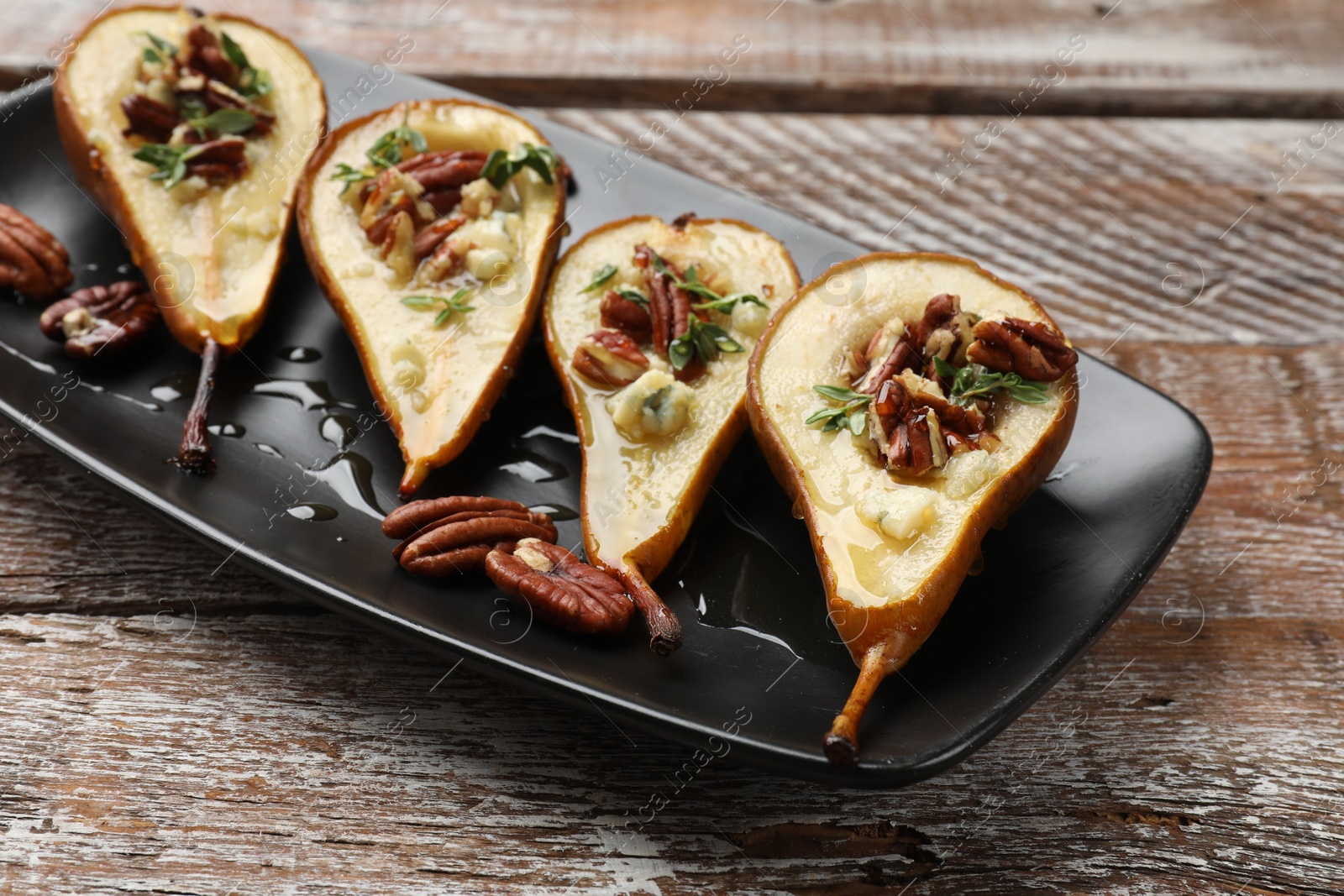 Photo of Tasty baked pears with nuts, blue cheese, thyme and honey on wooden table