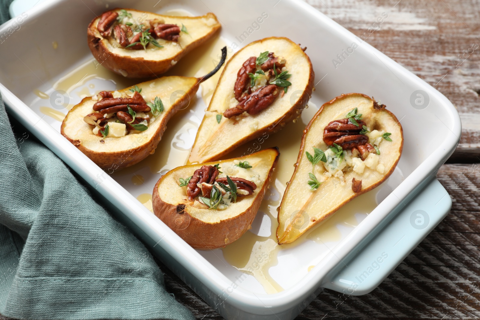 Photo of Tasty baked pears with nuts, blue cheese, thyme and honey in baking dish on wooden table