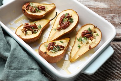 Tasty baked pears with nuts, blue cheese, thyme and honey in baking dish on wooden table