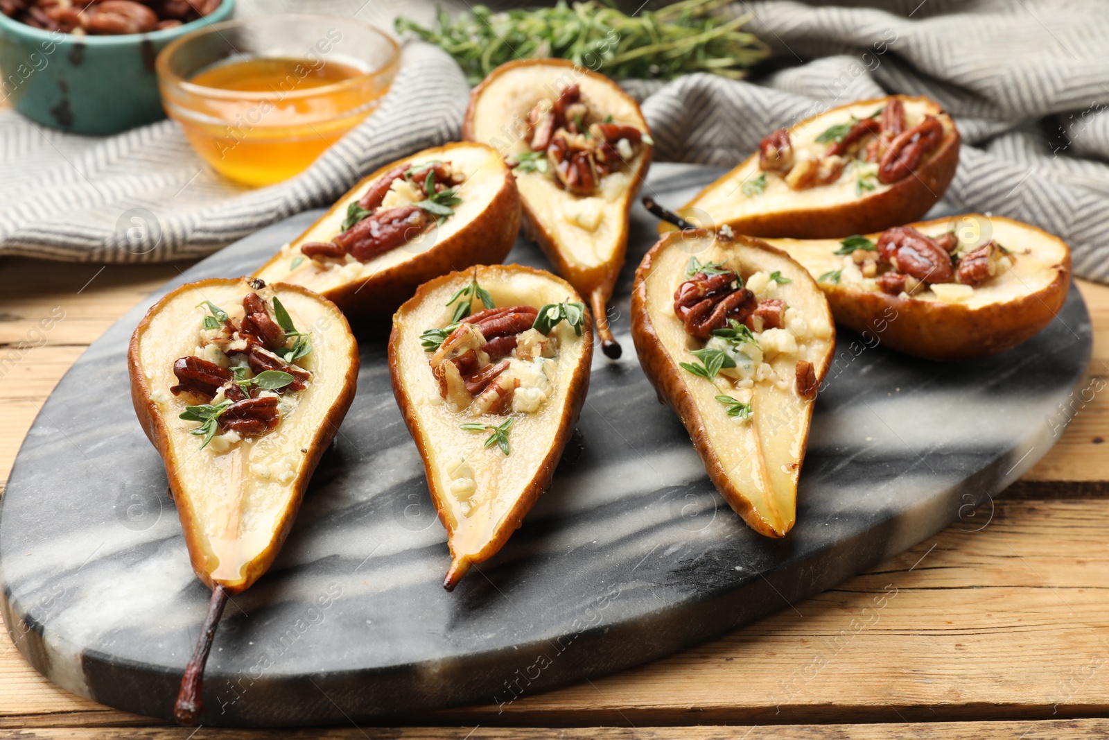 Photo of Tasty baked pears with nuts, blue cheese, thyme and honey on wooden table