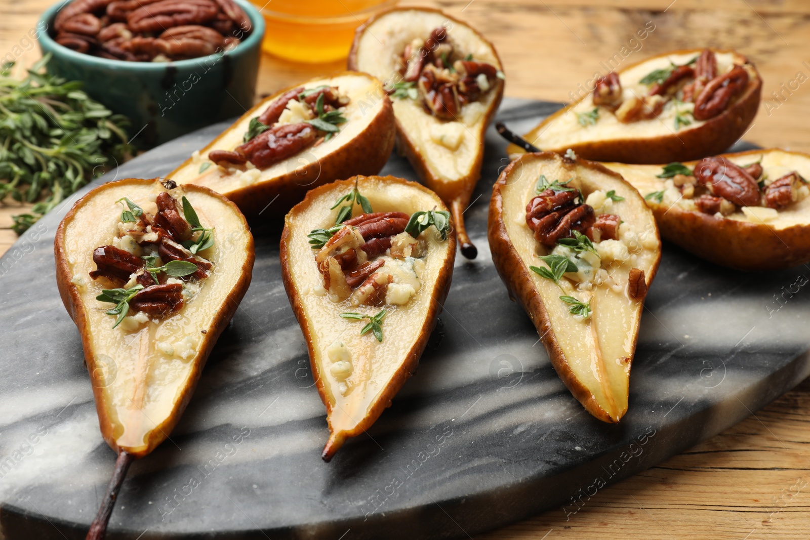 Photo of Tasty baked pears with nuts, blue cheese, thyme and honey on wooden table