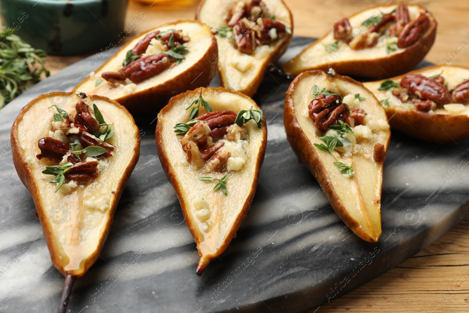 Photo of Tasty baked pears with nuts, blue cheese, thyme and honey on wooden table