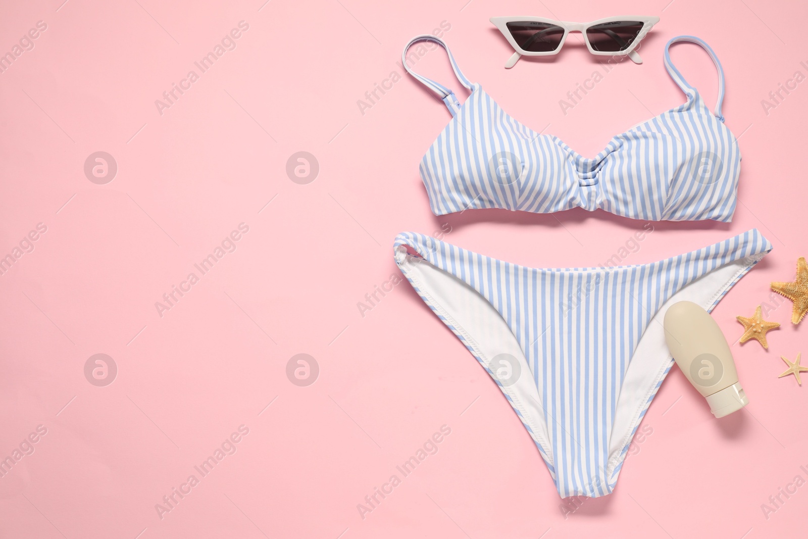 Photo of Striped swimsuit, sunscreen, sunglasses and starfishes on pink background, flat lay. Space for text