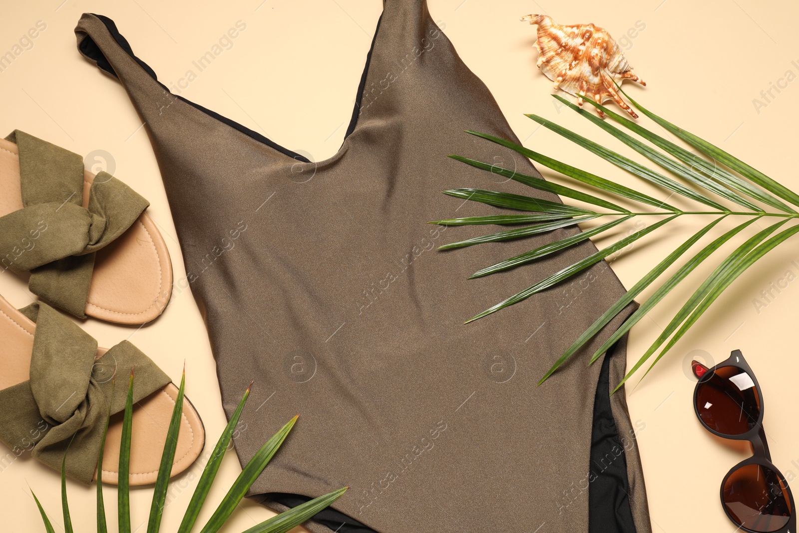 Photo of Beautiful swimsuit, palm leaves, sunglasses and slippers on beige background, flat lay