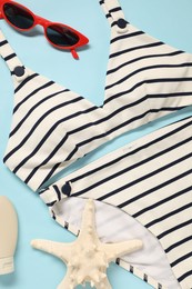 Photo of Striped swimsuit, sunglasses and starfish on light blue background, flat lay