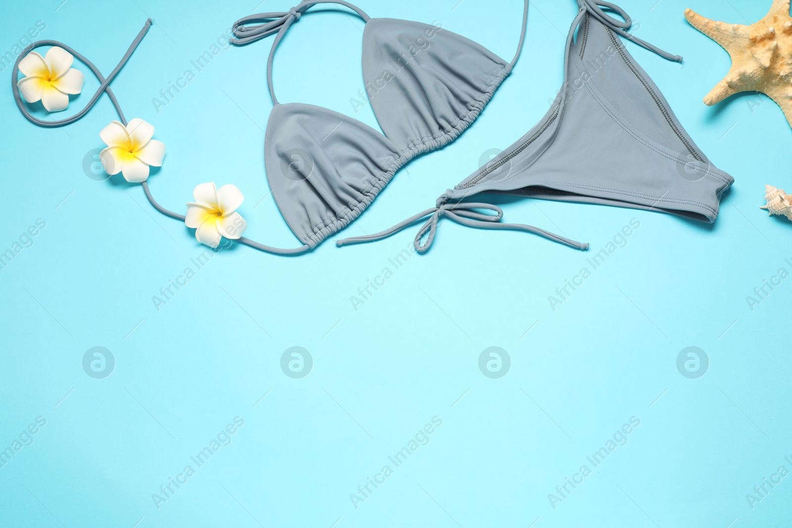 Photo of Flat lay composition with beautiful swimsuit, flowers and starfish on light blue background. Space for text