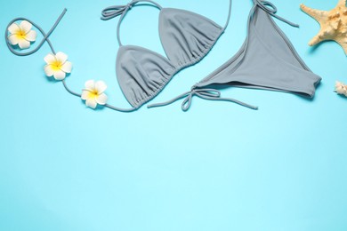 Flat lay composition with beautiful swimsuit, flowers and starfish on light blue background. Space for text