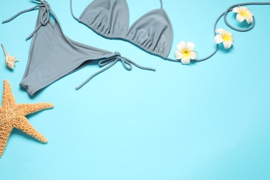Photo of Flat lay composition with beautiful swimsuit, flowers and starfish on light blue background. Space for text