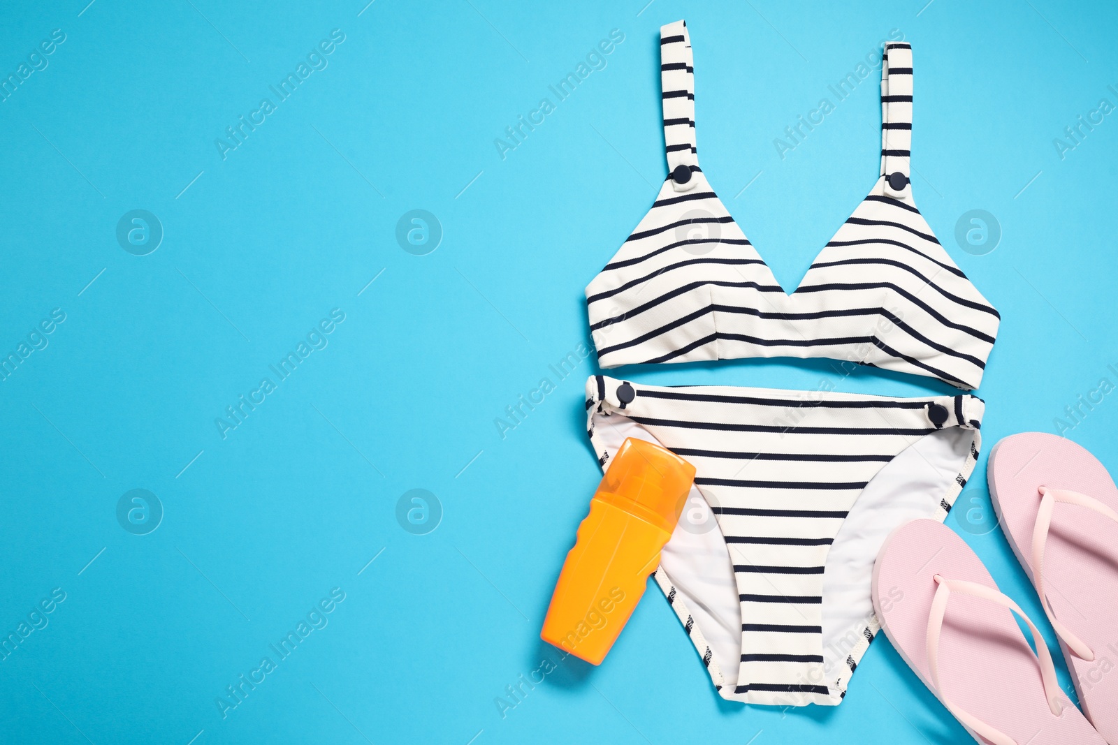 Photo of Striped swimsuit, flip flops and sunscreen on light blue background, flat lay. Space for text