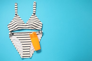 Striped swimsuit and sunscreen on light blue background, flat lay. Space for text