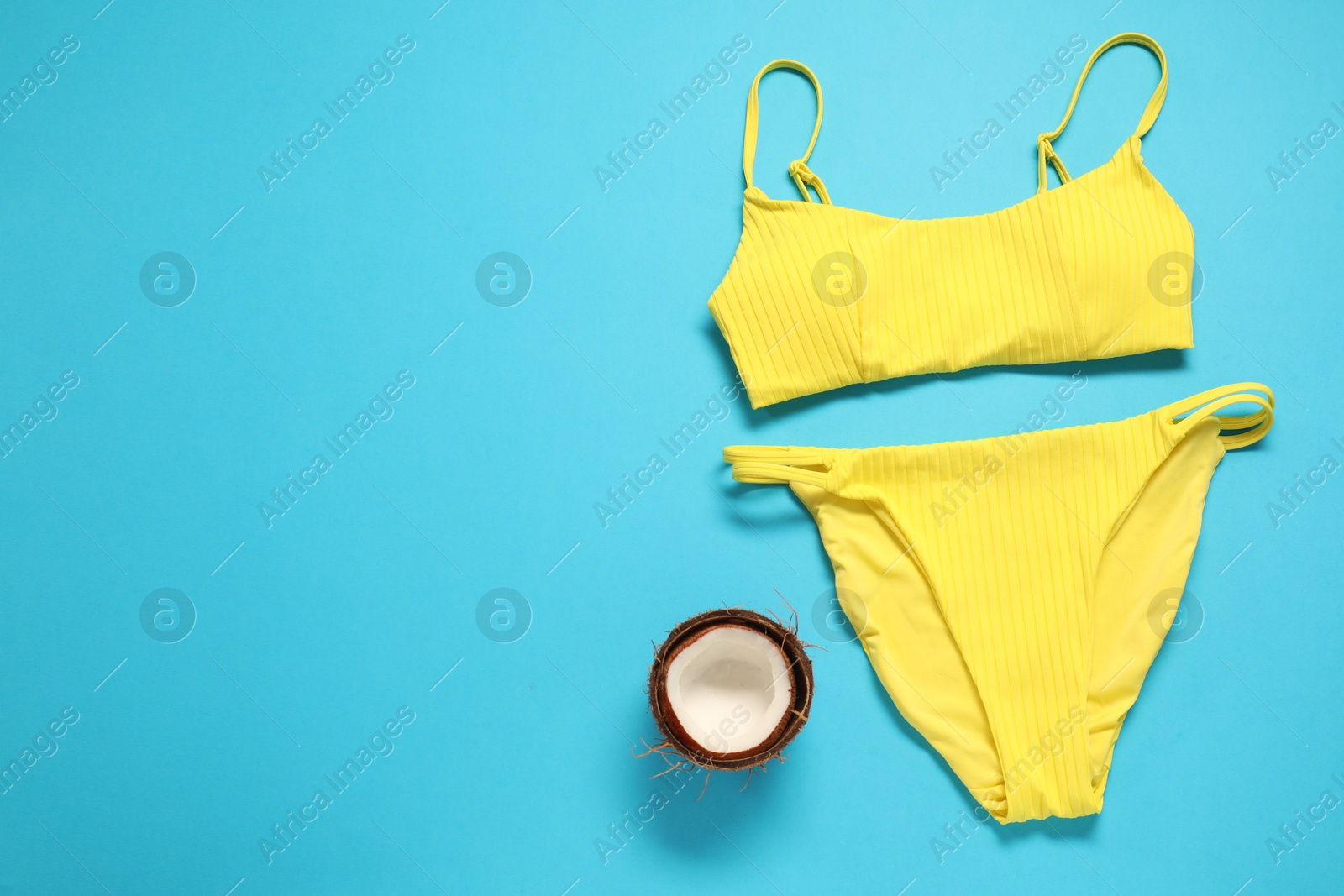 Photo of Yellow swimsuit and coconut on light blue background, flat lay. Space for text