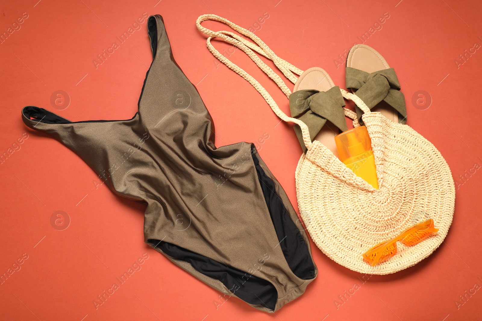 Photo of Beautiful swimsuit, bag, sunscreen, slippers and sunglasses on coral background, flat lay