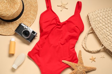 Photo of Red swimsuit, hat, sunscreen and camera on beige background, flat lay