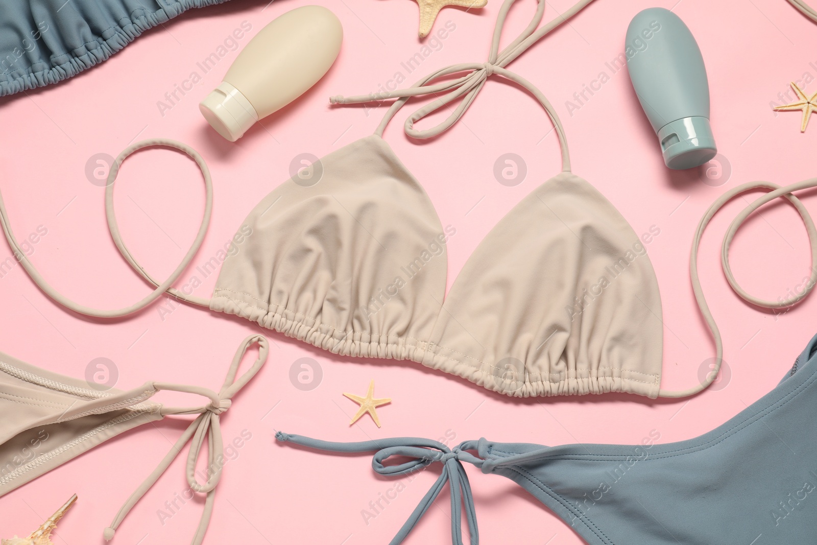 Photo of Beautiful swimsuits, seashells and sunscreens on pink background, flat lay