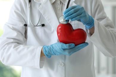 Photo of Doctor with stethoscope and red heart in clinic, closeup