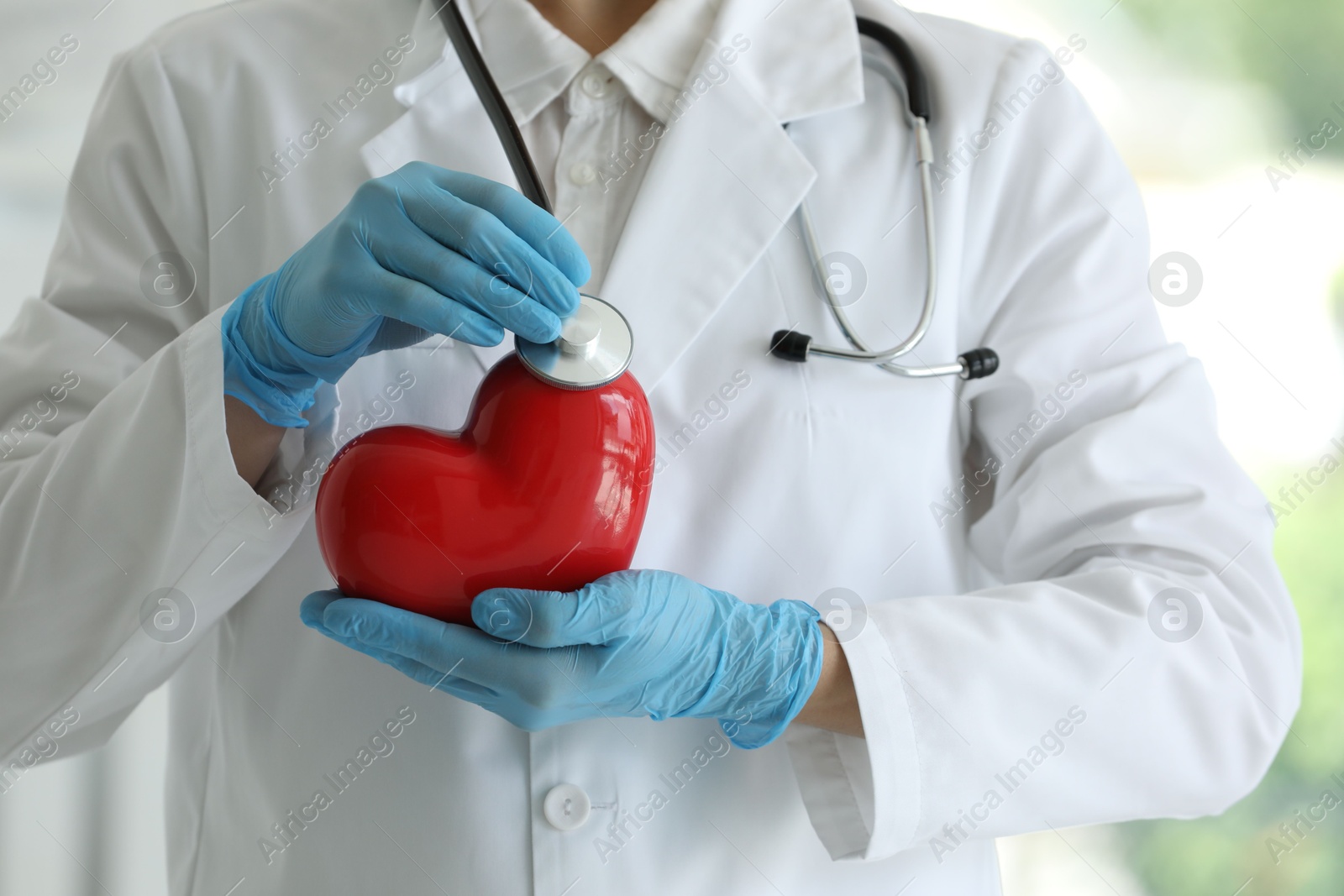 Photo of Doctor with stethoscope and red heart in clinic, closeup