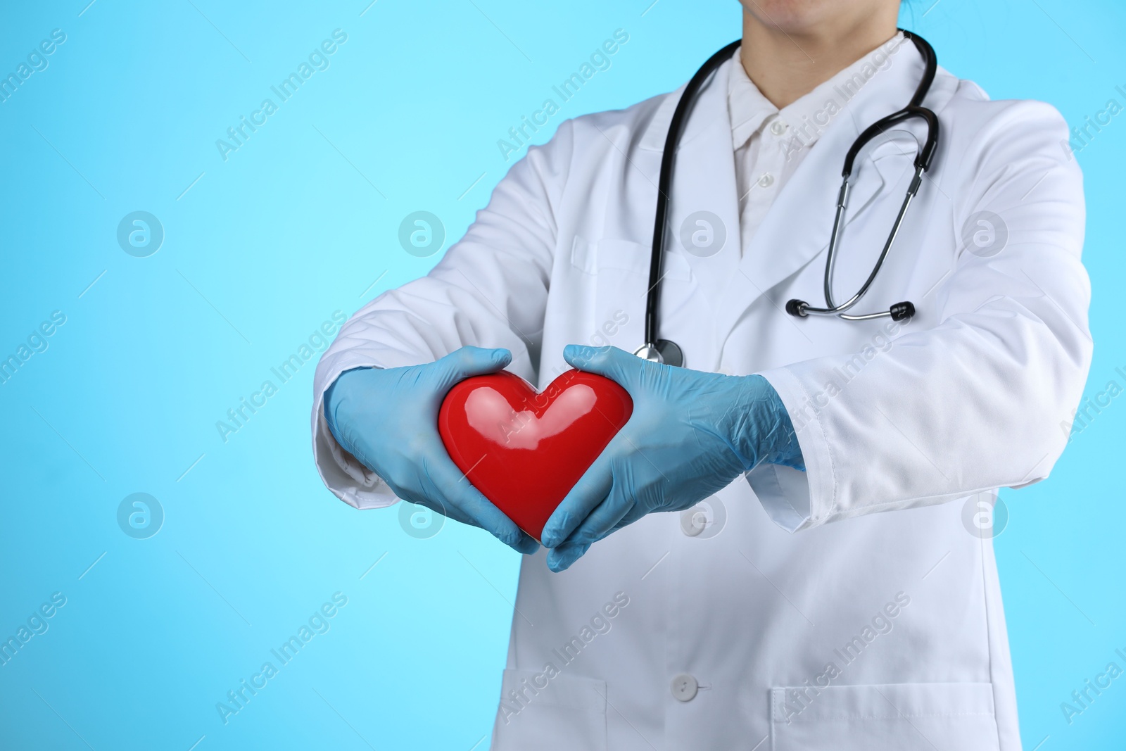 Photo of Doctor with red heart on light blue background, closeup. Space for text