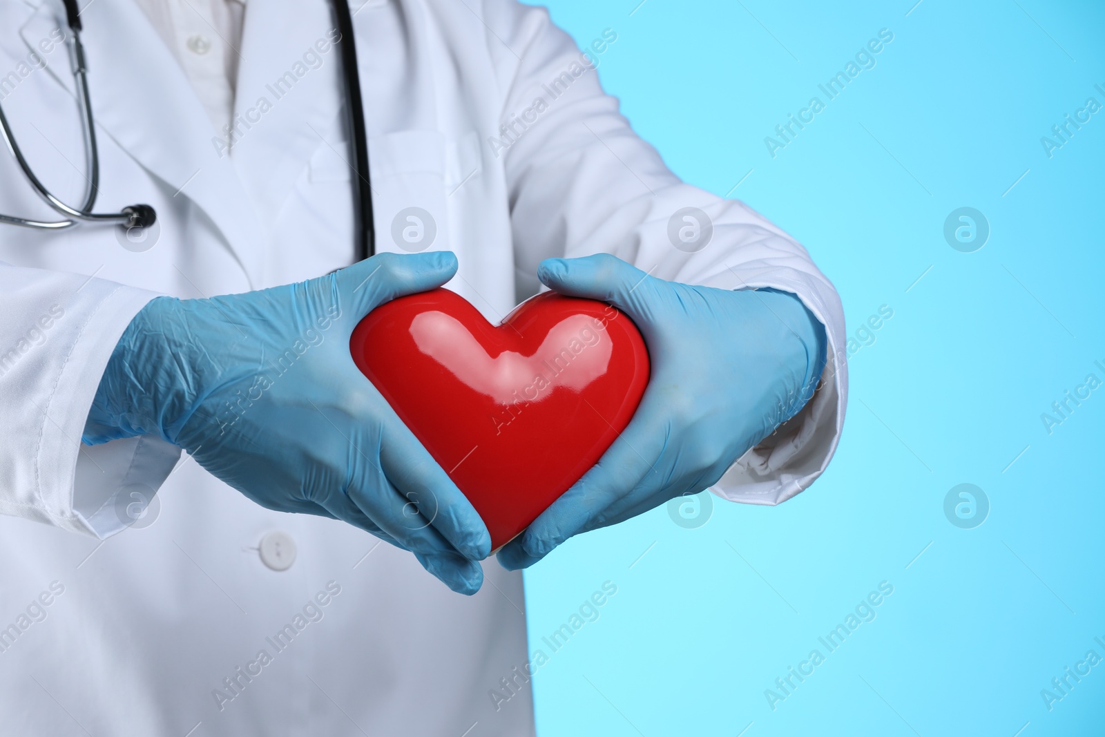 Photo of Doctor with red heart on light blue background, closeup