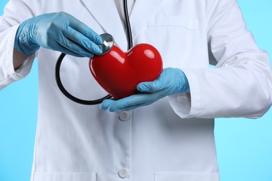 Photo of Doctor with stethoscope and red heart on light blue background, closeup