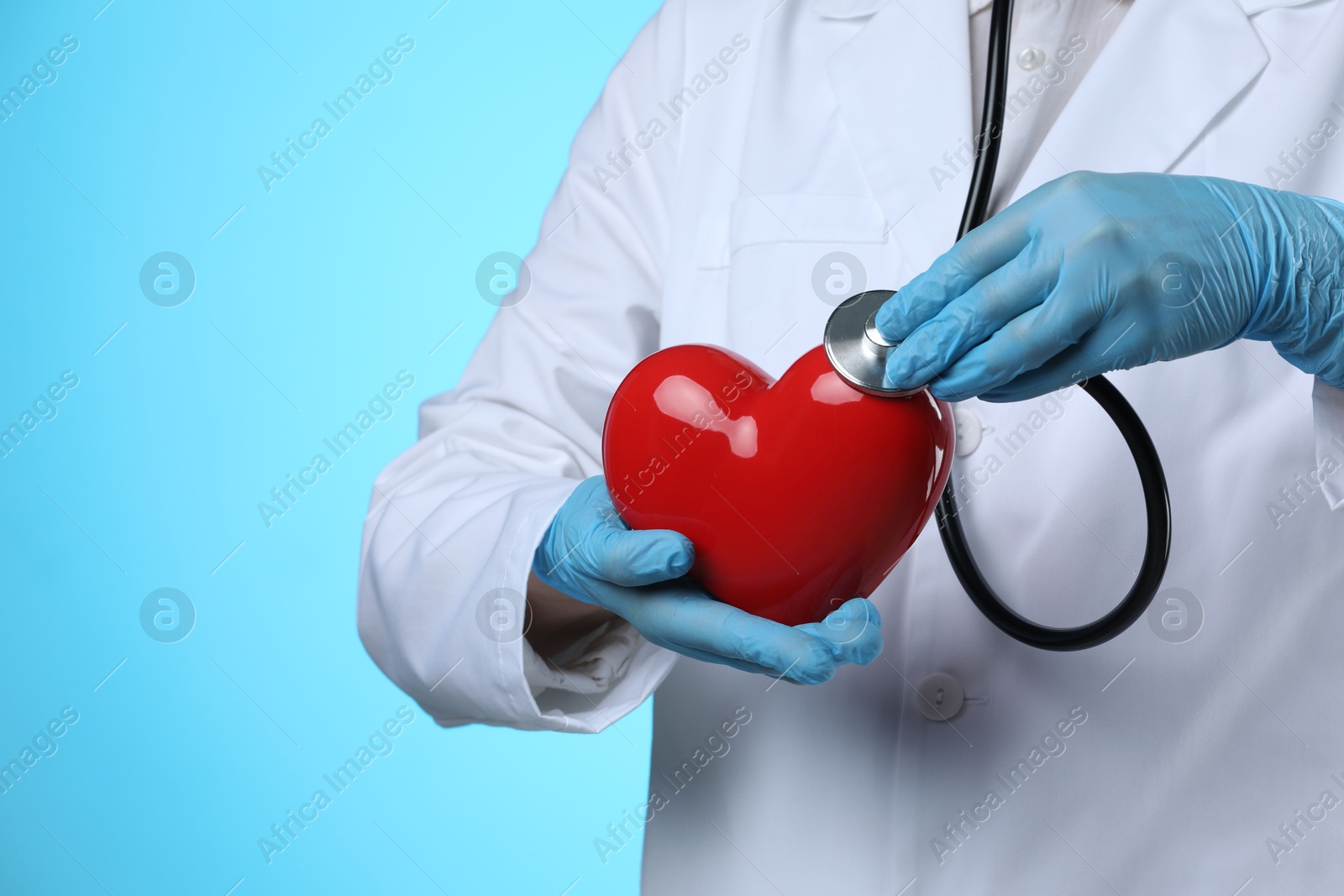 Photo of Doctor with stethoscope and red heart on light blue background, closeup