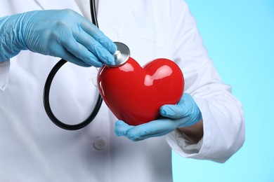 Photo of Doctor with stethoscope and red heart on light blue background, closeup