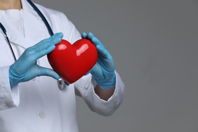 Doctor with red heart on grey background, closeup. Space for text