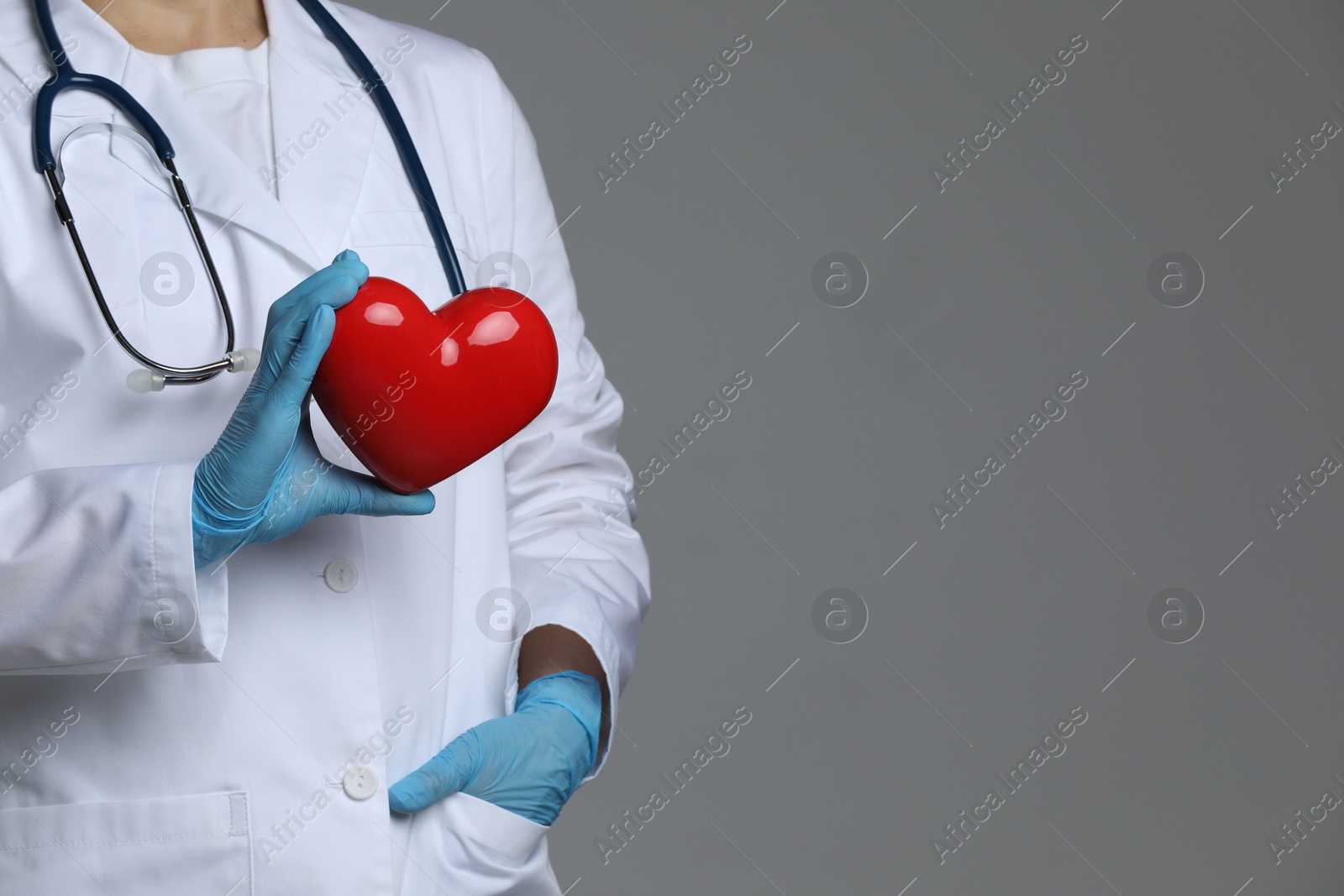 Photo of Doctor with red heart on grey background, closeup. Space for text