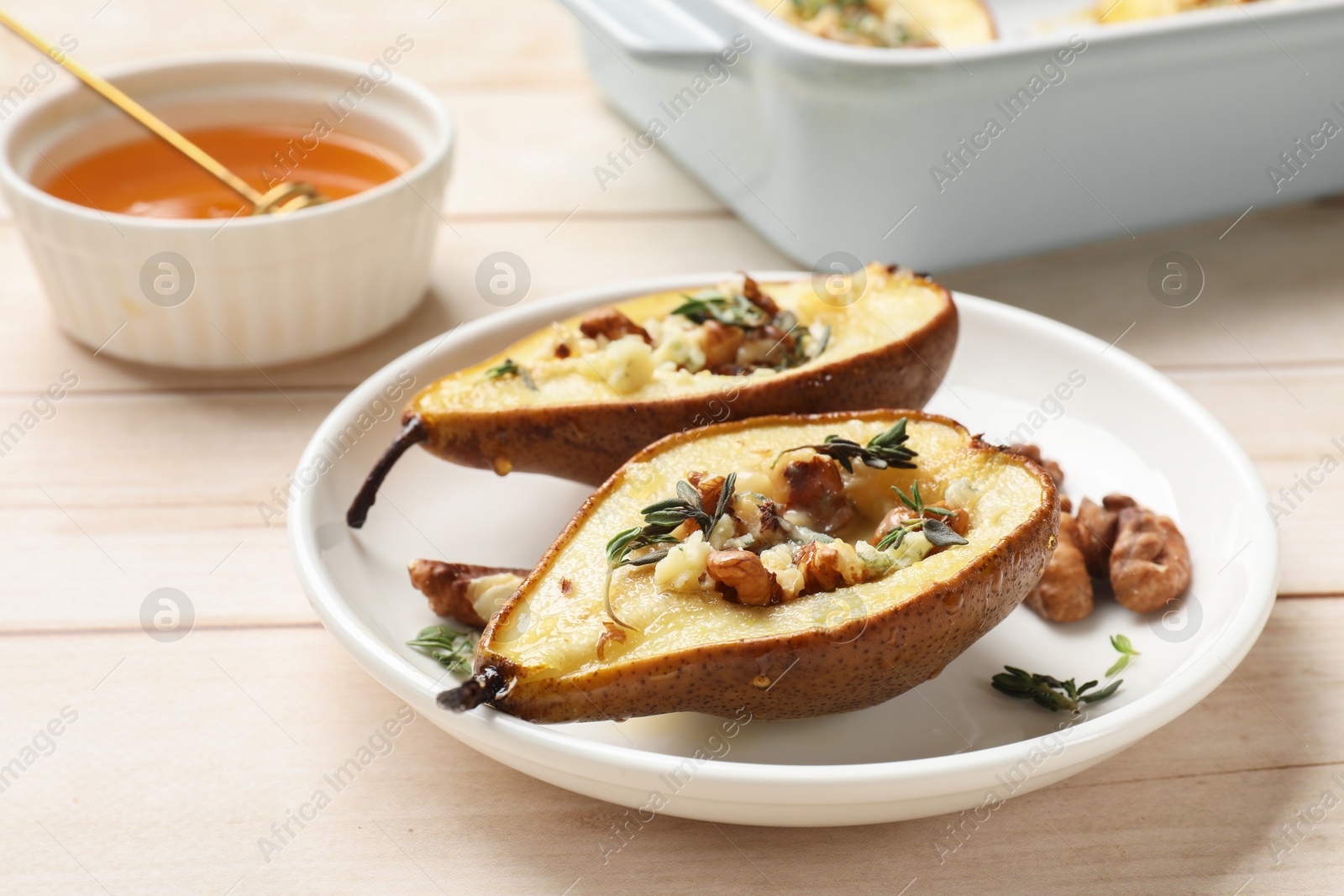 Photo of Tasty baked pears with nuts, blue cheese, thyme and honey on wooden table