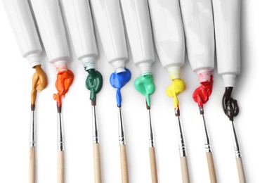 Photo of Tubes with colorful paints and brushes isolated on white, top view