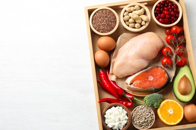 Tray with many different healthy food on white table, top view. Space for text