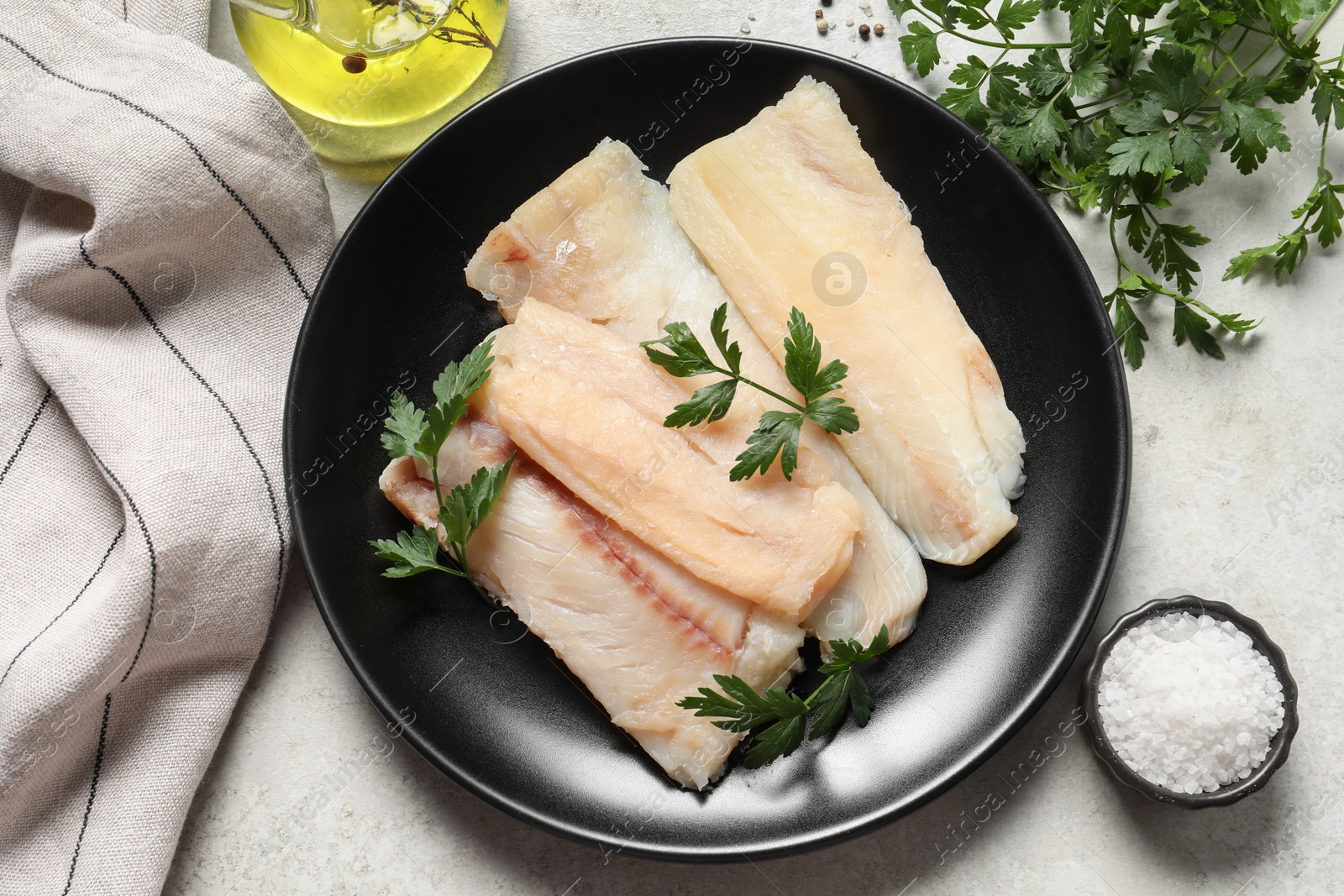 Photo of Plate with raw cod fish, parsley and salt on light table, flat lay