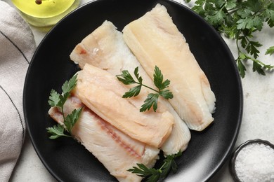 Photo of Plate with raw cod fish, parsley and salt on light table, flat lay