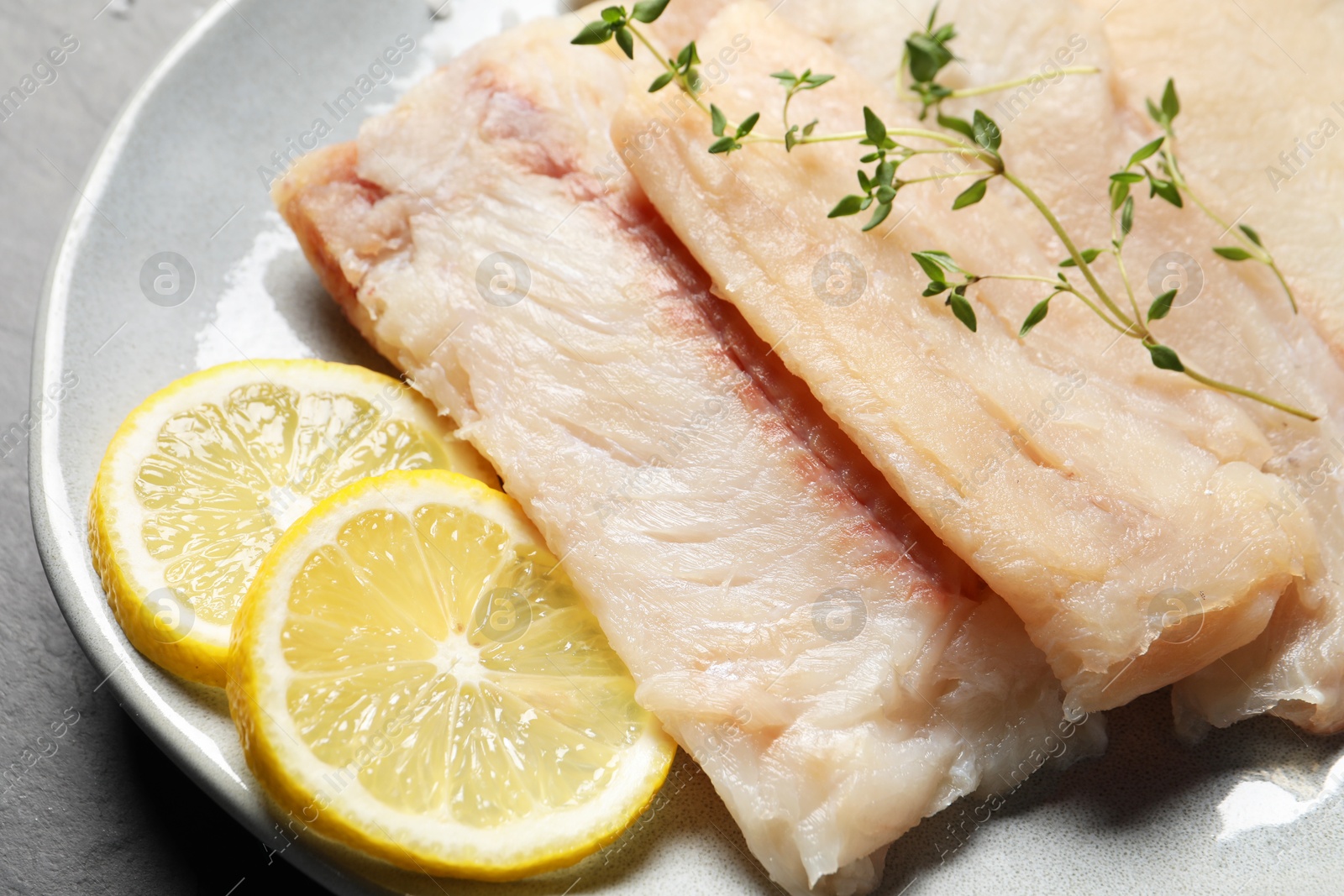 Photo of Plate with raw cod fish, microgreens and lemon on table, closeup