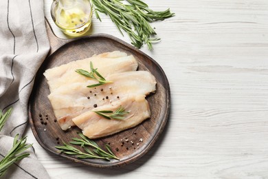 Photo of Raw cod fish, rosemary, oil and spices on white wooden table, flat lay. Space for text