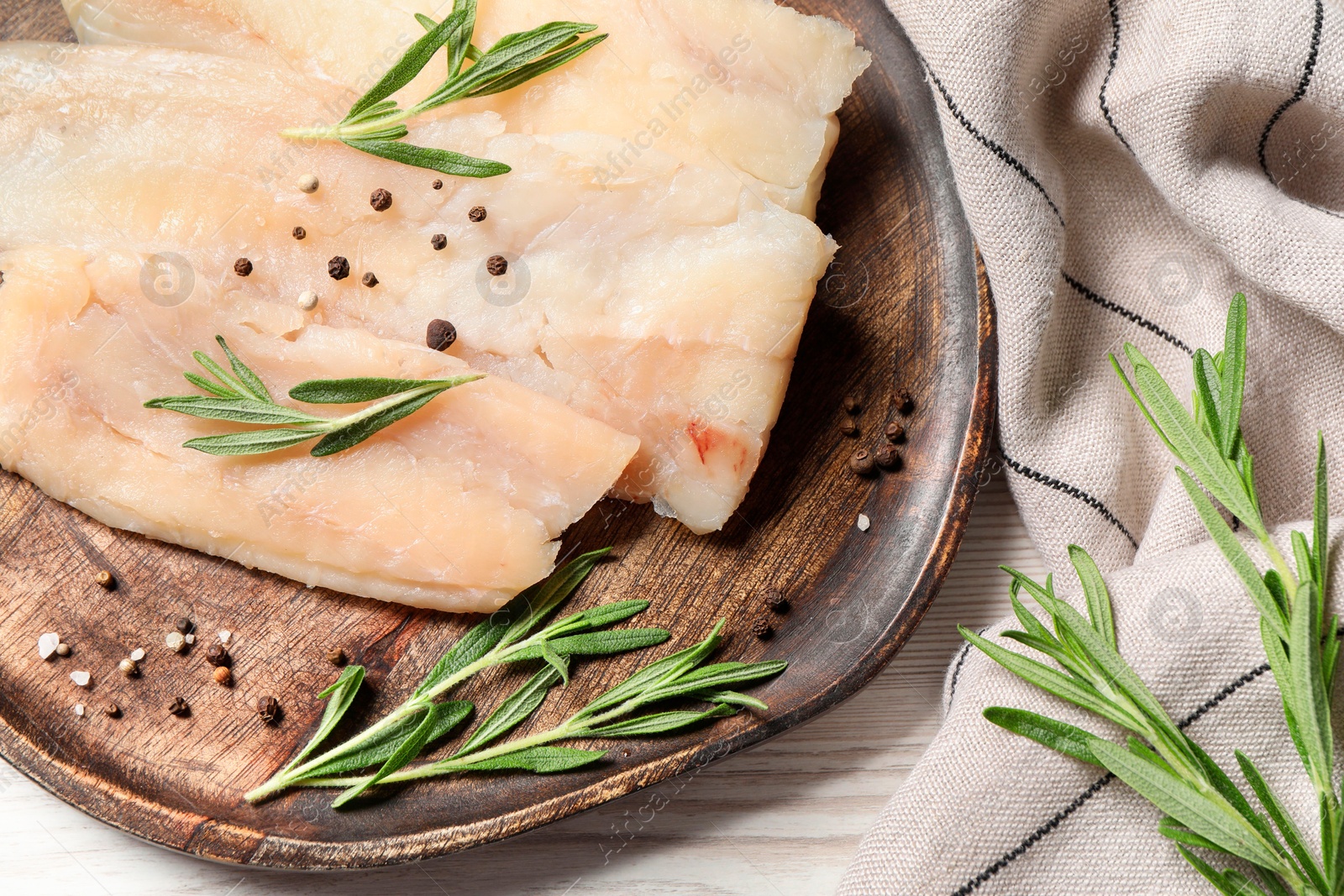 Photo of Raw cod fish, rosemary and spices on white wooden table, top view