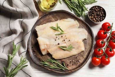 Raw cod fish, rosemary, tomatoes and spices on white wooden table, flat lay