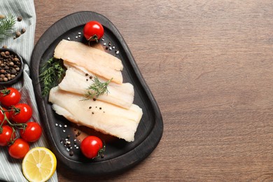 Raw cod fish, dill, lemon, tomatoes and spices on wooden table, top view. Space for text