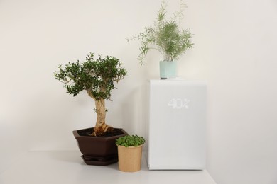 Modern air humidifier and houseplants on white table