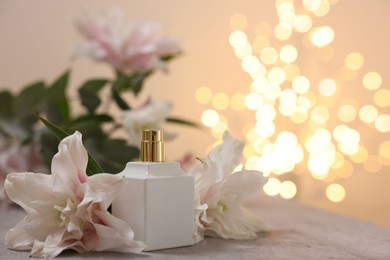 Photo of Bottle of perfume and beautiful lily flowers on table against beige background with blurred lights, closeup. Space for text