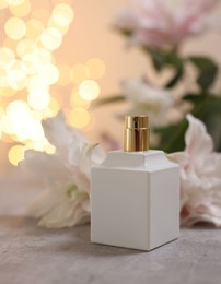 Photo of Bottle of perfume and beautiful lily flowers on table against beige background with blurred lights, closeup