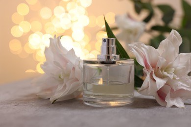 Photo of Bottle of perfume and beautiful lily flowers on table against beige background with blurred lights, closeup