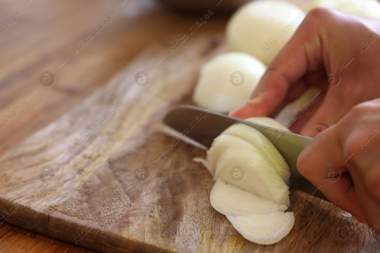 Photo of Woman cutting fresh ripe onion on wooden board, closeup. Space for text