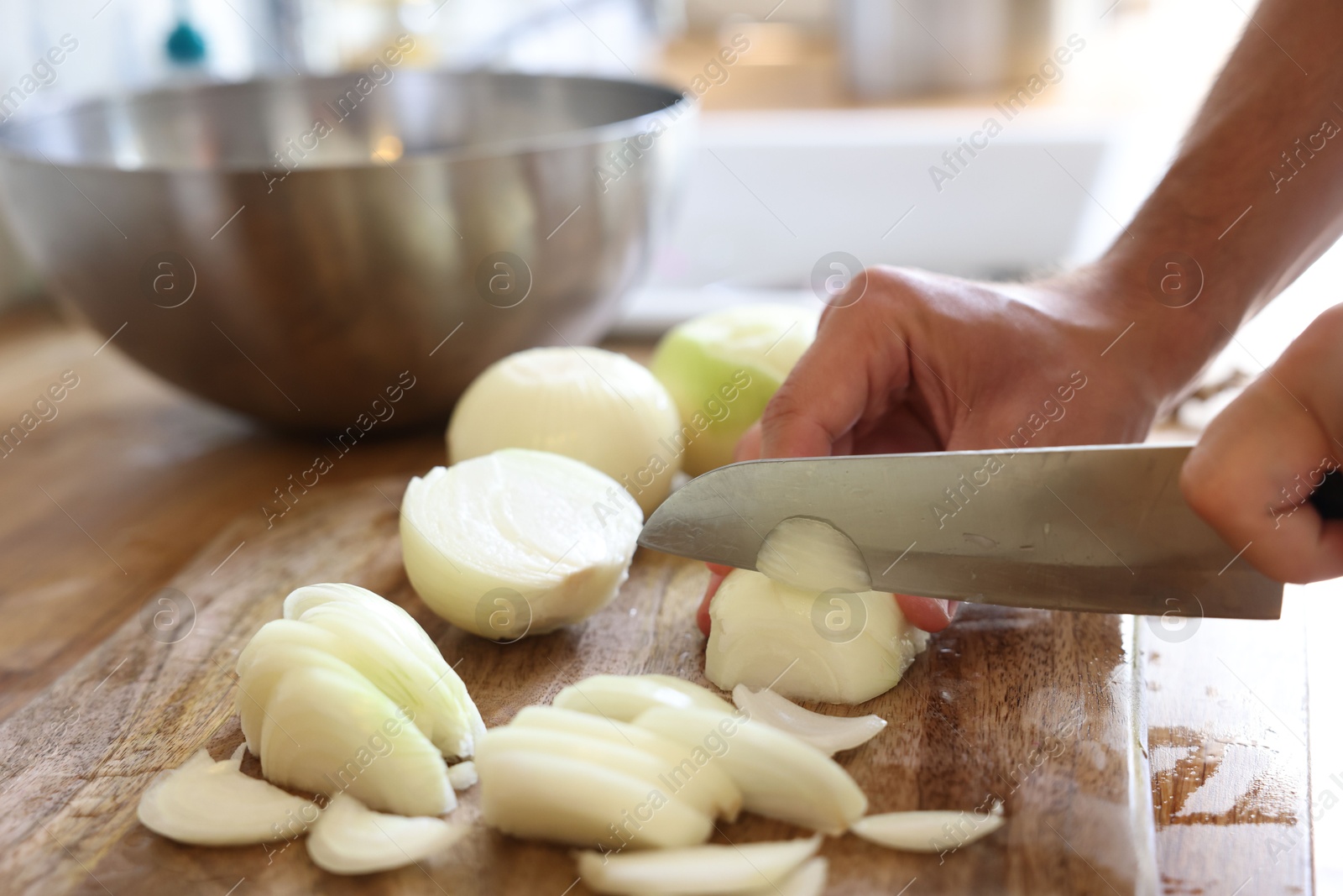 Photo of Woman cutting fresh ripe onion on wooden board indoors, closeup