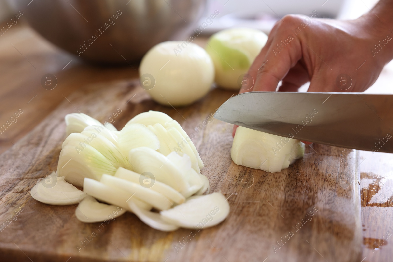 Photo of Woman cutting fresh ripe onion on wooden board, closeup