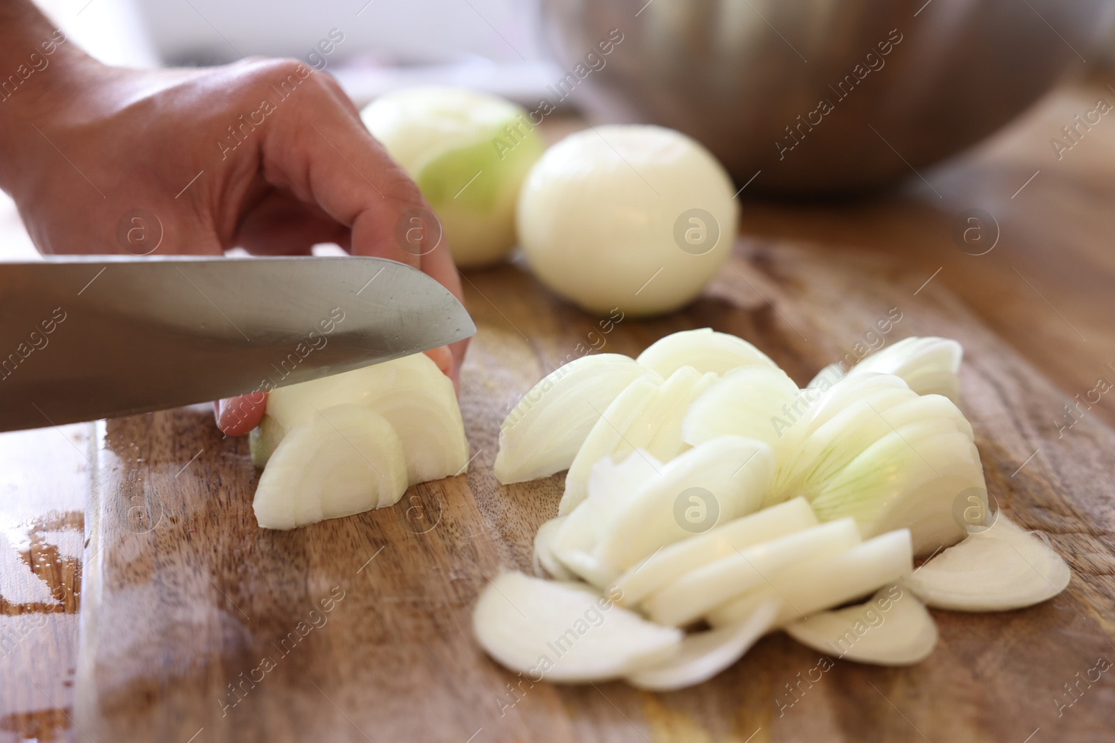 Photo of Woman cutting fresh ripe onion on wooden board, closeup