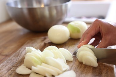 Photo of Woman cutting fresh ripe onion on wooden board, closeup